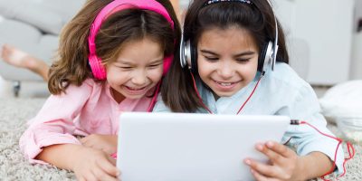 Portrait of beautiful young sisters listening to music with digital tablet.